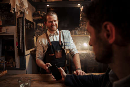 Caucasian bartender smiling at client grateful for support while client pays for drinks