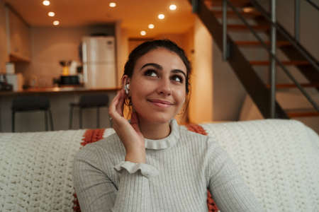 Caucasian female student relaxing on sofa listening to music with earphonesの写真素材