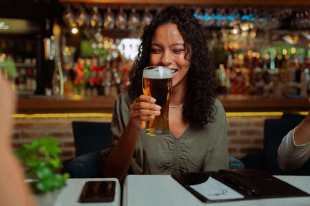 African American female enjoying beer while out for dinner with friends