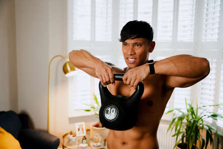 Asian male lifting kettlebells at home workoutの写真素材