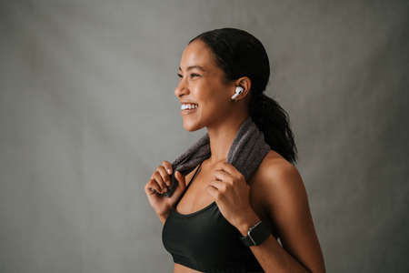 Multiethnic female listening to ear pods towel wrapped around her shoulders