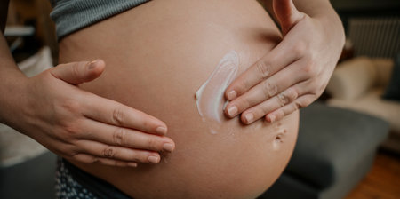 Close up pregnant female gently rubbing in cream on her bellyの写真素材