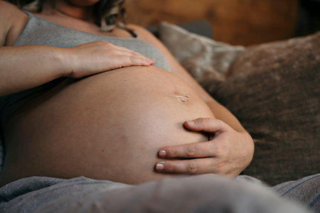 Close up of pregnant woman relaxing on her sofa cradling her bellyの写真素材