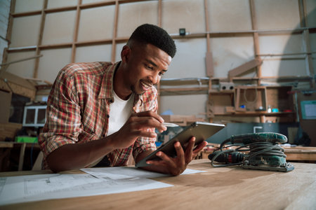 Smart African man working on tablet in wood factoryの写真素材
