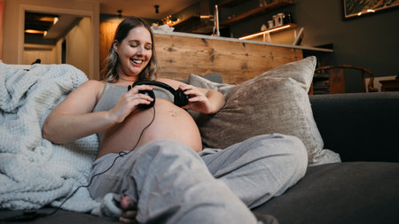 Close up of mother to be sitting on her sofa smiling listening to music .の写真素材