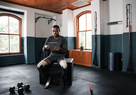 Man with prosthetic leg sits on gym bench, looks at tabletの写真素材