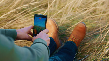 Capturing Natures Beauty: A Person Sitting in a Field of Grass While Taking a Photo with a Smartphone, Showcasing the Serenity of the Outdoor Environment and Relaxationの写真素材