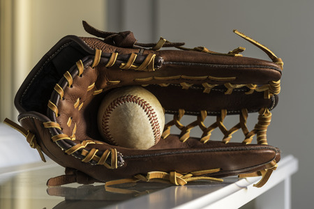 Close-up of a used baseball ball inside brown, leather baseball glove on plain, grey background.の写真素材