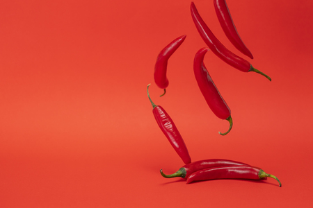 Image of red narrow long spicy chili peppers falling down on the red backgroundの写真素材