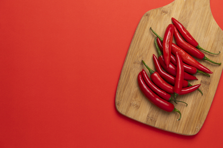 Group of red hot chilli peppers on the wooden chopping board on red backgroundの写真素材