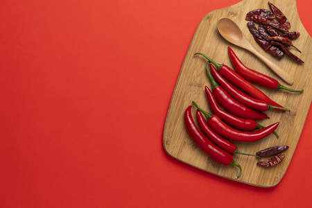 Groups of red chilli peppers and dried asian hot capsicum on the wooden chopping board on red backgroundの写真素材