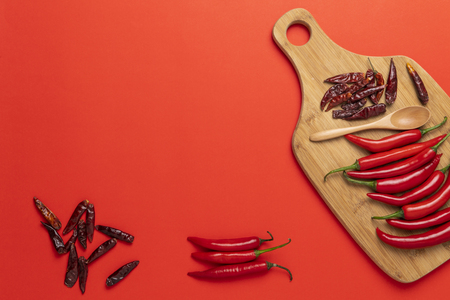 Groups of red chilli peppers and dried asian hot capsicum on the wooden chopping board on red backgroundの写真素材