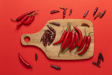 Groups of red chilli peppers and dried asian hot capsicum on the wooden chopping board on red backgroundの写真素材
