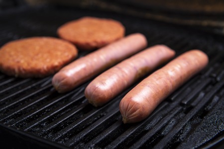 Fresh uncooked barbecue sausages, burgers and bread ready to be grilled, sitting on a grillの写真素材