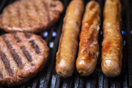 Pork sausages and burgers grilling on a portable BBQ, close up of the grill, meat and fireの写真素材