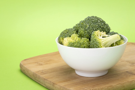 Broccoli pieces in white bowl sitting on wooden chopping boardの写真素材