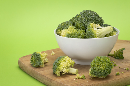 Broccoli pieces in white bowl sitting on wooden chopping boardの写真素材