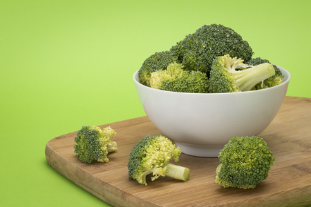 Broccoli pieces in white bowl sitting on wooden chopping boardの写真素材