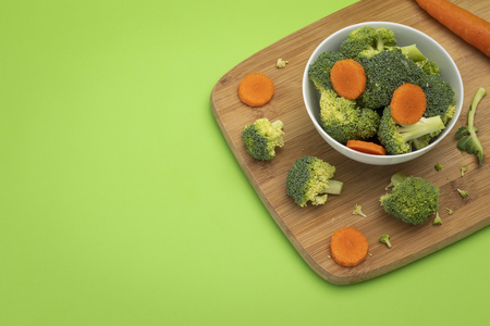 Broccoli and carrot mixed in white bowl sitting on wooden chopping boardの写真素材