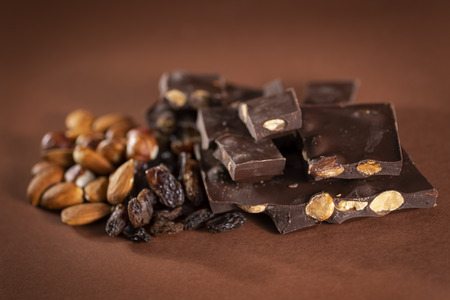 Stack of dark chocolate pieces with roasted almonds and raisins isolated on brown backgroundの写真素材