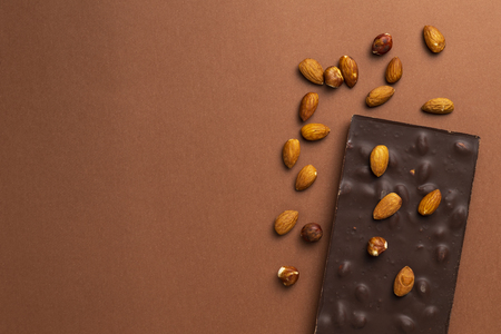 Dark chocolate bar with roasted almonds scattered around on brown backgroundの写真素材