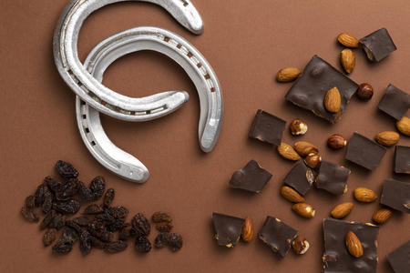 Dark chocolate pieces with roasted almonds and raisins scattered around horse shoes on brown backgroundの写真素材
