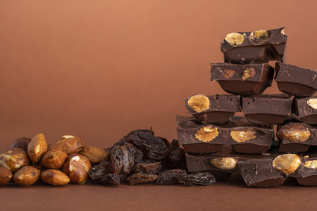 Stack of dark chocolate pieces with roasted almonds and raisins isolated on brown backgroundの写真素材