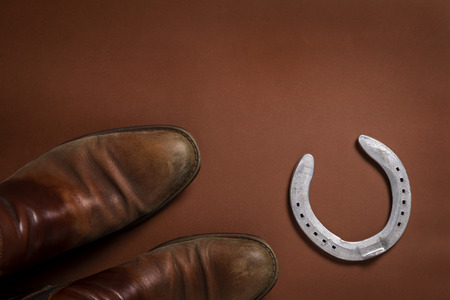 Horseshoe and a pair of leather shoes isolated on a brown background with copy spaceの写真素材