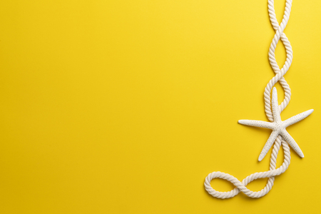 Summer time concept with starfish and rope on a plain yellow backgroundの写真素材