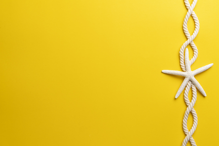 Summer time concept with starfish and rope on a plain yellow backgroundの写真素材