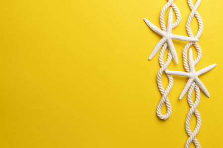Summer time concept with starfish and rope on a plain yellow backgroundの写真素材