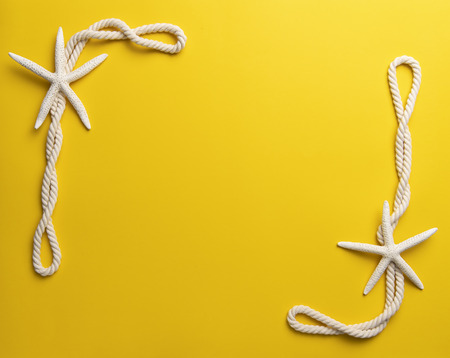Summer time concept with starfish and rope on a plain yellow backgroundの写真素材