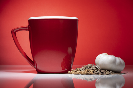 Red mug with small pile of tea and garlic isolated on the red backgroundの写真素材