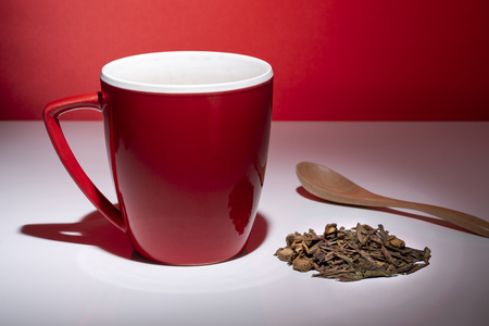 Red mug with small pile of tea and a spoon isolated on the red backgroundの写真素材