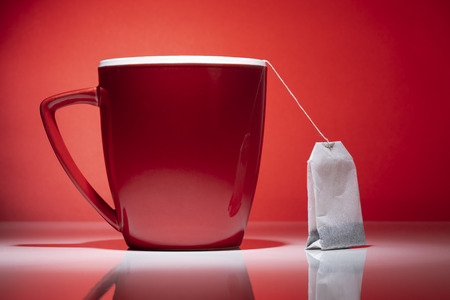 Red mug and a tea bag isolated on the red backgroundの写真素材