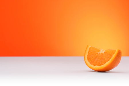 A piece of orange isolated on an orange and white background with space for textの写真素材