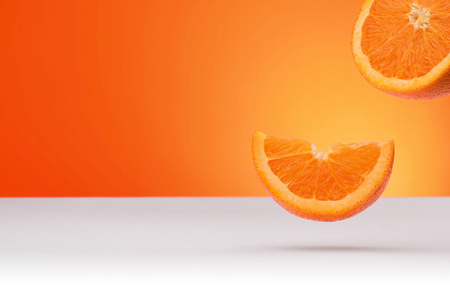 Floating oranges isolated on an orange and white background with space for textの写真素材