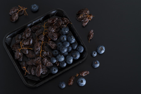 Bunch of dried sultanas and blue berries on a tray isolated on black backgroundの写真素材