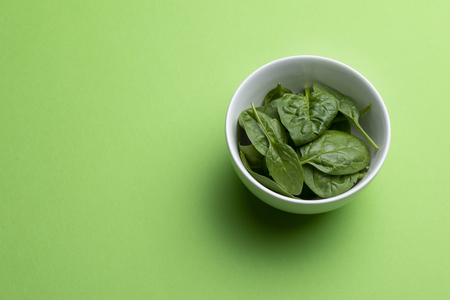 Babe spinach leaves in white porcelain bowl isolated on green background