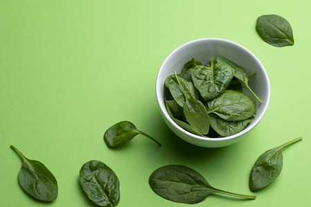 Babe spinach leaves in white porcelain bowl isolated on green backgroundの写真素材
