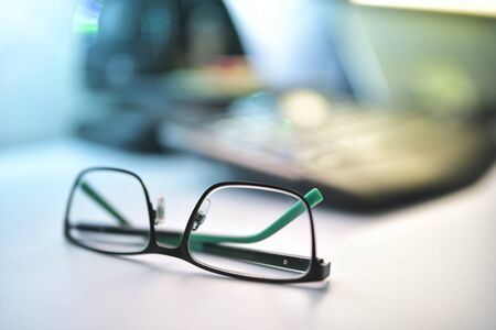 Close up image of black and green eyeglasses on the desk with blur backgroundの写真素材
