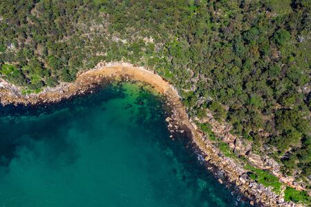 Aerial drone shot of the north coastline of Ku-ring-gai Chase National Park, green tree forest and the rocky coastline with clear turquoise water taken from above, birds eye view landscapeの写真素材