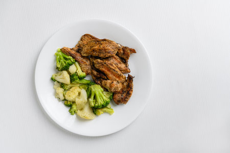 Grilled broccoli, cauliflower and chicken breast on a white plateの写真素材