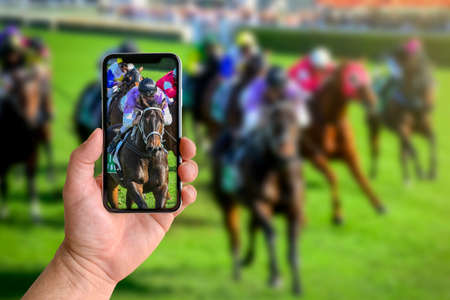 Man taking photo of horse racing with mobile phone with blurred background, closeup of hand. Space...