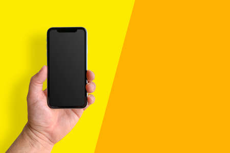 Man holding mobile phone with blank screen on yellow and orange background, closeup of hand. Space for textの写真素材