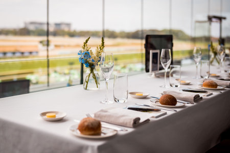 Table with glasses, cutlery and food with the horse racing track in the backgroundの写真素材