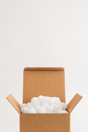 Cardboard box isolated on the white background filled with packing peanuts. Copy space.