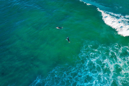 Top drone aerial view over group of surfers in the shallow green watersの写真素材