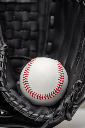 Closeup of a white baseball ball with red stitches inside baseball gloveの写真素材