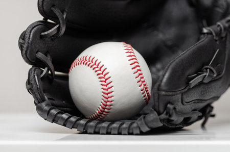 Closeup of a white baseball ball with red stitches inside baseball gloveの写真素材